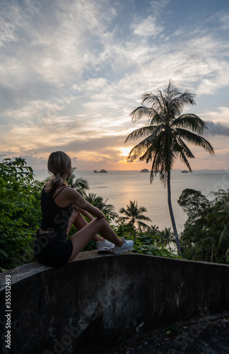 Silhouette of woman sitting alone on the hill with a coconut palm trees and enjoys sea on a horizon in a sunset. Vacation and travel concept on a island. Beautiful sunsets on a Samui island.