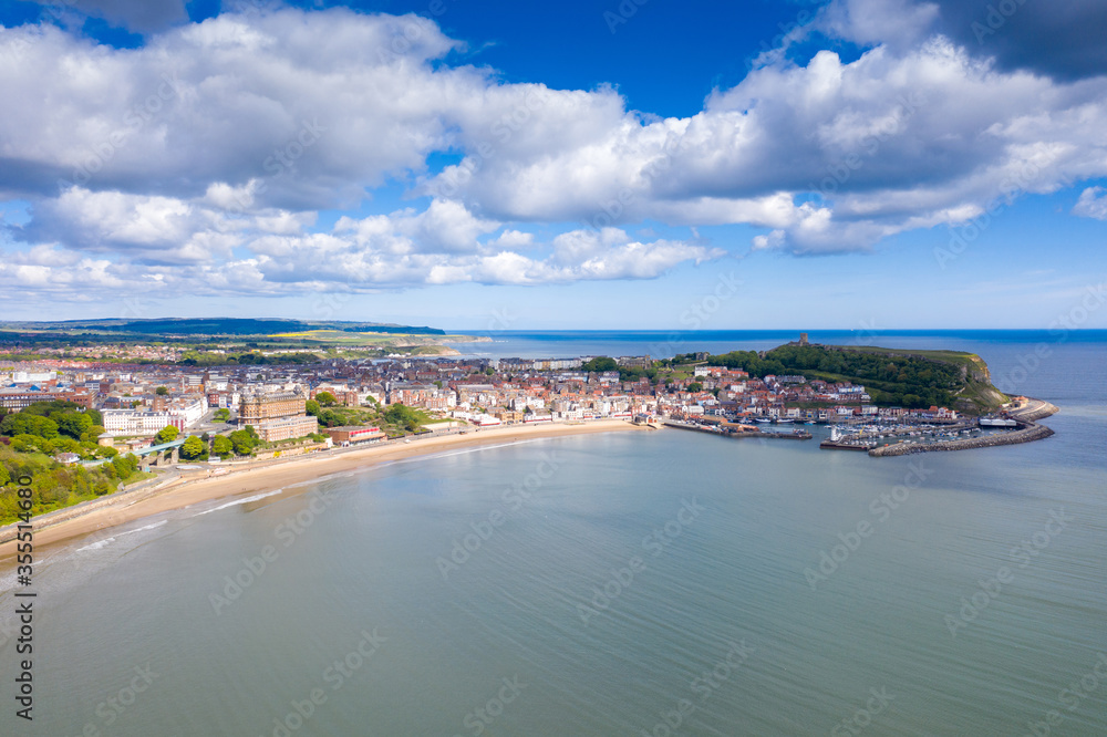 Aerial photo of the town centre of Scarborough in East Yorkshire in the UK showing the coastal beach and harbour with boats and the Scarborough Castle on a bright sunny summers day
