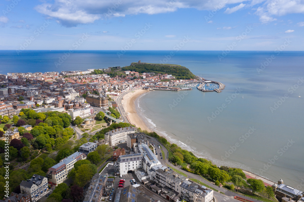 Aerial photo of the town centre of Scarborough in East Yorkshire in the UK showing the coastal beach and harbour with boats and the Scarborough Castle on a bright sunny summers day Aerial photo of the town centre of Scarborough in East Yorkshire in the UK showing the coastal beach and harbour with boats and the Scarborough Castle on a bright sunny summers day