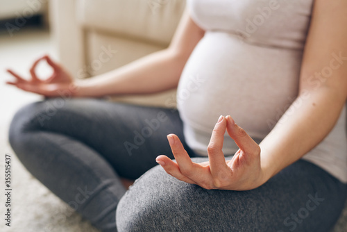 Hand and leg bent in knee of young pregnant woman sitting in pose of lotus