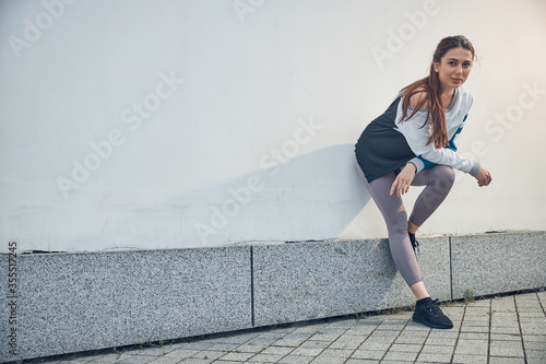 Sporty long-haired female standing by a wall