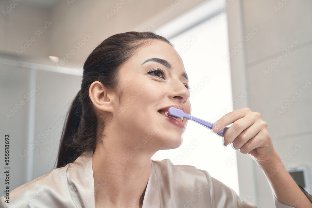 Pleasant young woman cleaning her teeth at bathroom Pleasant young woman cleaning her teeth at bathroom