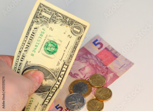 a hand holding US dollar bills and some brazilian real and coins in the background . business finance shopping concept.
