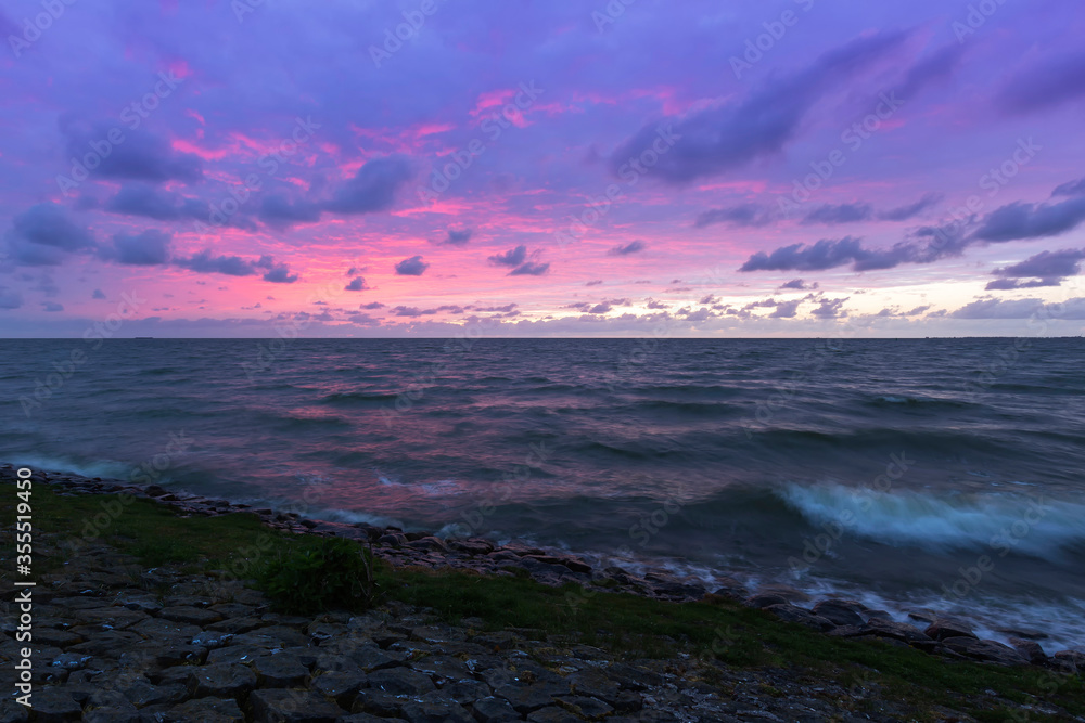 Fototapeta premium Holland - Sunset over the stormy sea. A stone rampart jutting out into the sea. in the foreground sand and green grass.