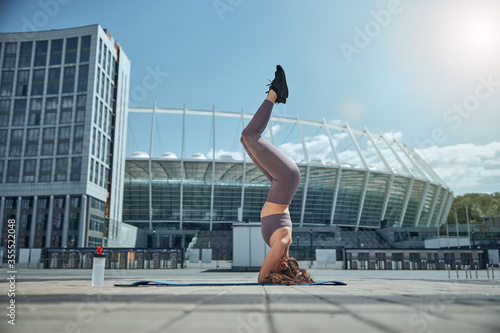 Strong young woman performing a headstand outdoors