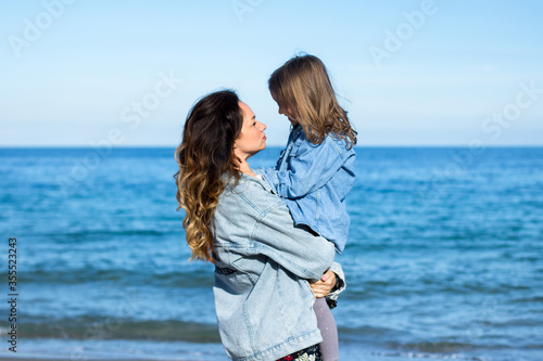 young woman in jeans jacket keeps on the hands little girl on the beach