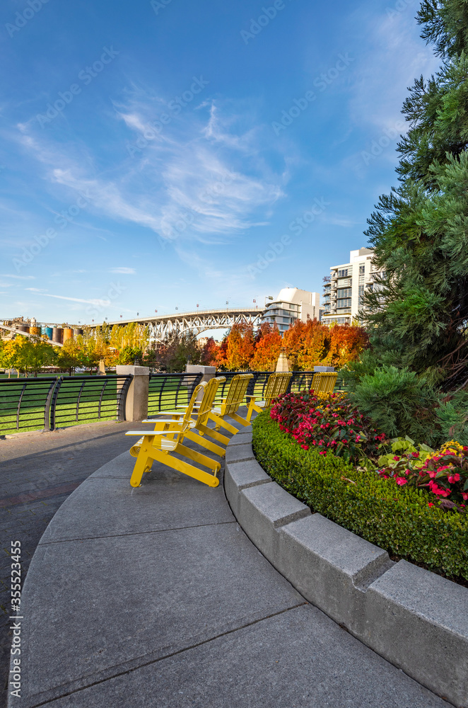 A shot of a row of yellow metal chairs in George Wainborn Park, Vancouver, in the fall with the Burrard bridge in the distance 