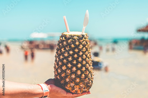 Hand holding pineapple cocktail on a ocean and blue sky background