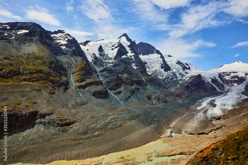 Panoramic view at Pasterze Glacier Grossglockner among austrian Alps mountains summits blue sky clouds.