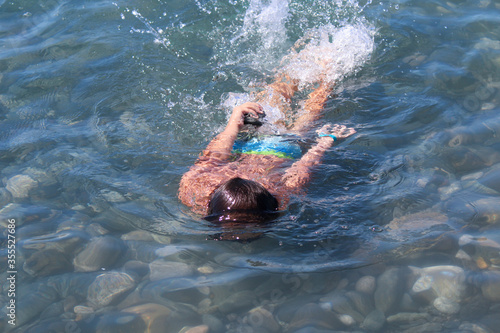 A boy swims under water in shallow water. Water splashes and rocks on the bottom. Summer vacation at the sea.