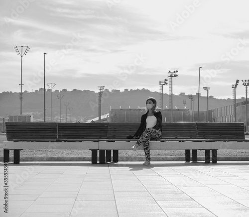 woman wearing mask for protect virus corona covid19 for sitting at park. Woman relaxing in a spring park in a protective surgical face mask sitting on a bench . monochome . covid 19