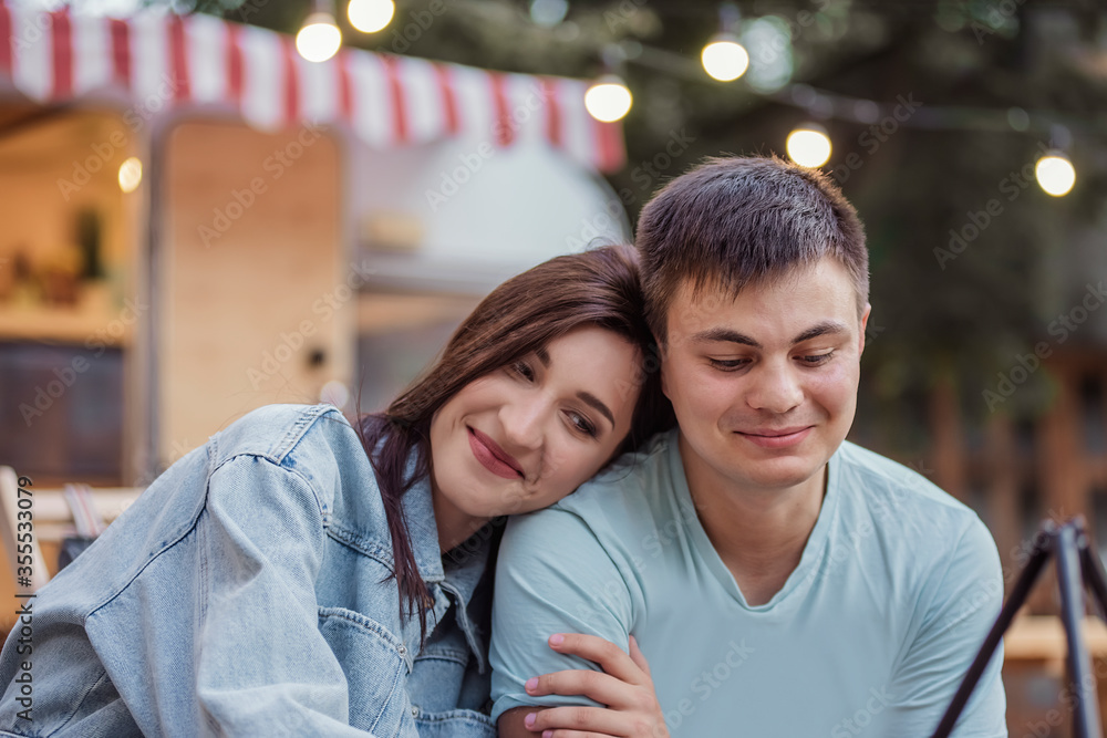 A beautiful young couple of newlyweds in jeans are sitting by their trailer, covered with a blanket, hugging, kissing by a burning fire. Honeymoon at a camping picnic, relaxation in the countryside. A beautiful young couple of newlyweds in jeans are sitting by their trailer, covered with a blanket, hugging, kissing by a burning fire. Honeymoon at a camping picnic, relaxation in the countryside.