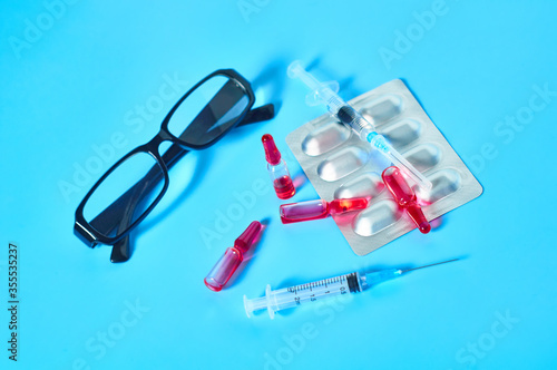Different medicaments near glasses on blue background. Healthcare and medical concept