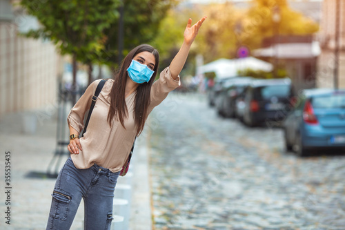 Woman with protective mask standing alone on empty street and waiting for bus or taxi transport. Virus or air pollution concept.