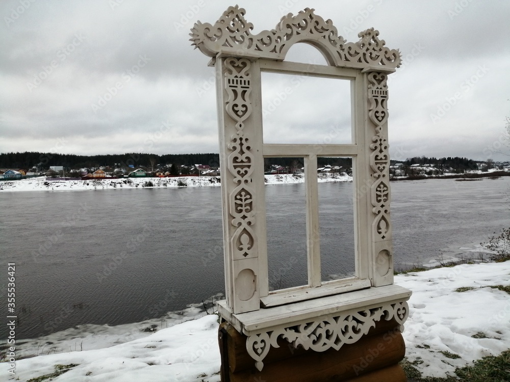 View on the bank of wide river with a wooden white pattrned window in cloudy winter weather Russia