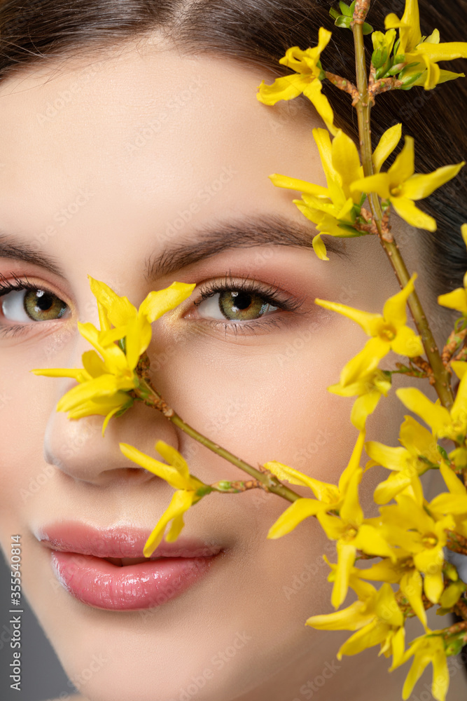 Girl with a beautiful make-up. Near her are beautiful blooming yellow flowers. Looking at the camera.Professional makeup and cosmetology care. Girl with a beautiful make-up. Near her are beautiful blooming yellow flowers. Looking at the camera.Professional makeup and cosmetology care.