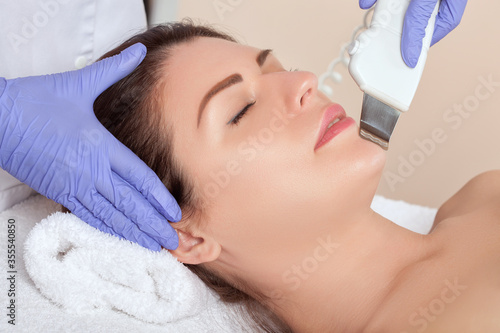 The cosmetologist makes the ultrasound cleaning procedure of of the facial skin of a beautiful woman in a beauty salon. Cosmetology and professional skin care.