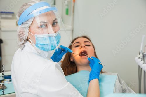Female dentist curing teeth cavity in blue gloves and protective mask. Dentist caries treatment at dental clinic office. People, medicine, stomatology and health care concept