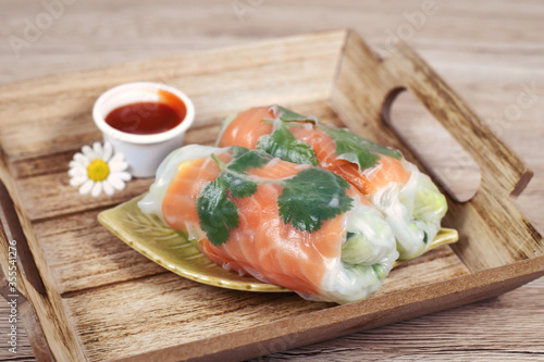 Traditional Vietnamese spring rolls filled with salmon, avocado, salad and rice noodles on wooden tray