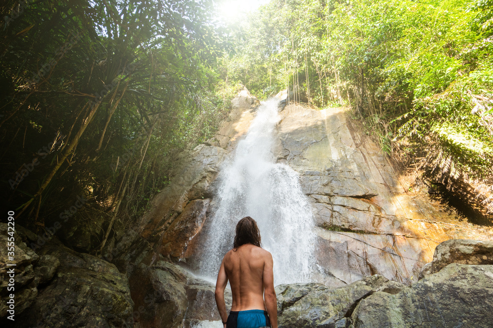 Man with a long hair is enjoy in lagoon of huge tropical waterfall in jungle. Travel concept. Man with a long hair is enjoy in lagoon of huge tropical waterfall in jungle. Travel concept.