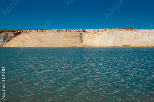 Small waves on blue water and a sandy beach. Pond on a sand quarry.