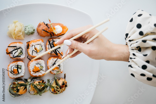 Rolls and sushi on a white plate. Hand with sushi sticks. 