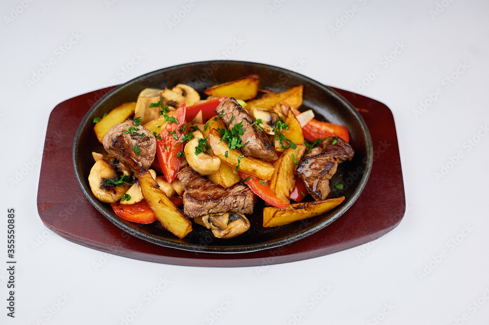 hot cast-iron frying pan with meat and potatoes on a white background hot cast-iron frying pan with meat and potatoes on a white background