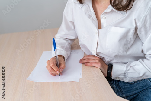 Woman at work. Writing some papers on the desk. Home office or small company situation with real people. Female is wearing white shirt. Cropped photo.