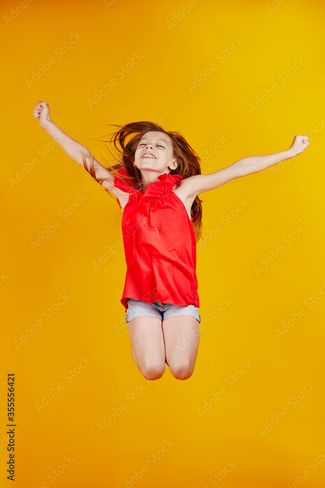 jolie jeune enfant fille caucasienne aux cheveux longs châtains sautant de joie sur fond jaune de studio