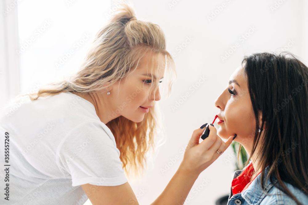 Two girl friends spend time making make-up to each other. One beautiful girl put lipstick on lips of another pretty girl Two girl friends spend time making make-up to each other. One beautiful girl put lipstick on lips of another pretty girl