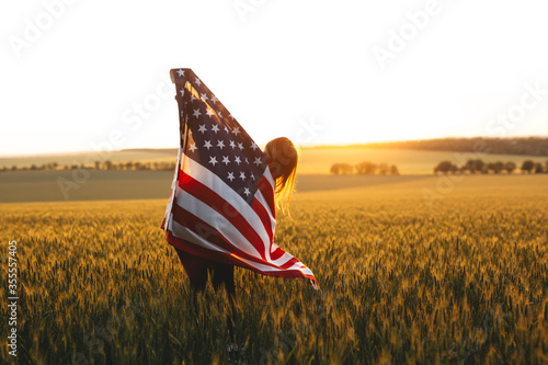 Фотография Beautiful girl with American flag in a wheat field at sunset