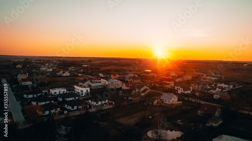 View to the Ukrainian village from above with some modern houses, few ponds and some empty fields at the background. View during the sunset. Spring time. Golden hour time. Sun in the frame.