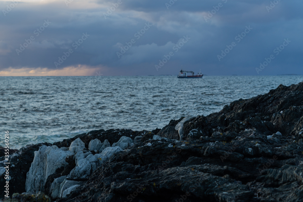 Boat going into storm with rock in foreground