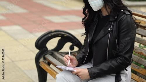 Young woman with the mask writing something in the notepad