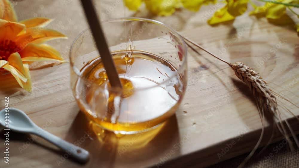 Pouring and stirring golden liquid bee honey in transparent jar with wooden stick, natural product production in countryside. Apiculture activity, vitamins and healthy eating Pouring and stirring golden liquid bee honey in transparent jar with wooden stick, natural product production in countryside. Apiculture activity, vitamins and healthy eating