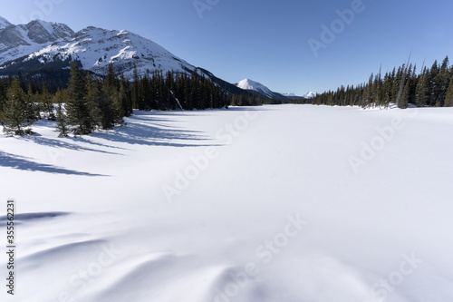 Winter alpine panorama with lake fully covered by snow, shot at Burstall Lakes, Kananaskis, Canadian Rockies, Alberta, Canada photo