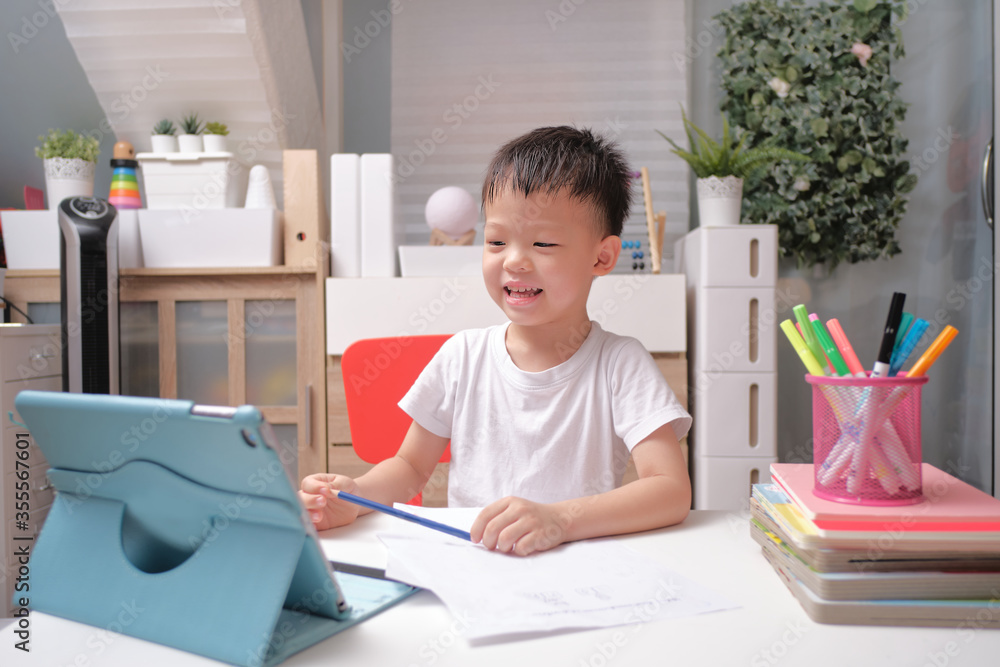 Asian schoolboy kid using tablet pc computer studying homework during his online lesson at home, Kindergarten closed during the Covid-19 health crisis, Distance learning, homeschooling concept Asian schoolboy kid using tablet pc computer studying homework during his online lesson at home, Kindergarten closed during the Covid-19 health crisis, Distance learning, homeschooling concept