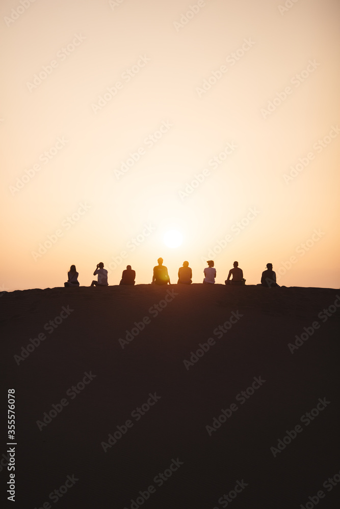 people sit on top of a dune in the desert and watch the sunset in warm colors