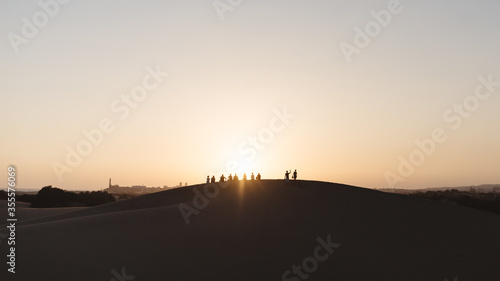 people sit on top of a dune in the desert and watch the sunset in warm colors