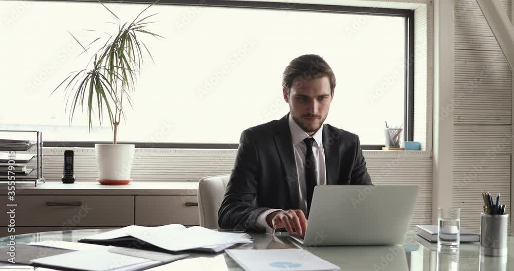 Successful satisfied young male company director wearing suit relaxing at workplace taking break after finishing computer work, chilling on chair, dreaming, feels peace of mind puts hands behind head. Successful satisfied young male company director wearing suit relaxing at workplace taking break after finishing computer work, chilling on chair, dreaming, feels peace of mind puts hands behind head.