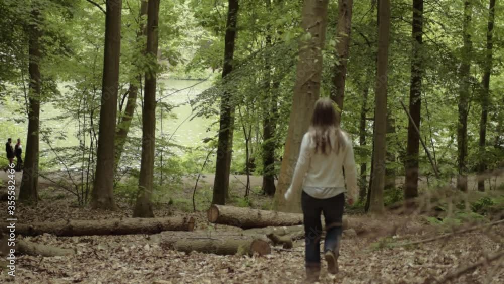 Woman walking through forest with felled logs with lake background wide landscape shot Woman walking through forest with felled logs with lake background wide landscape shot