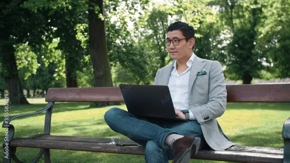 Young Business Man in Glasses Working on Laptop on a Park Bench. Young Business Man in Glasses Working on Laptop on a Park Bench.