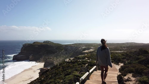 On a boardwalk at Cape of Good Hope, a girl walks with the wind blowing her hair in the bright contrasting light. photo