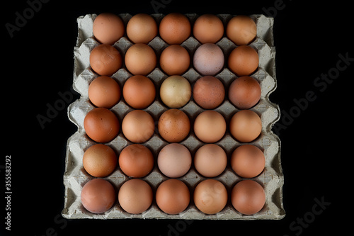 Chicken eggs in the egg tray isolated on the black background. Top view.