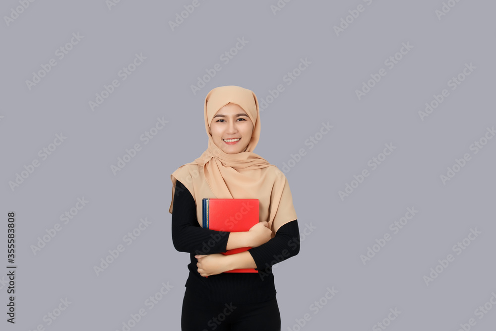 Young asian muslim woman smiling wearing hijab head scarf and holding carrying a quran over gray background. Young asian muslim woman smiling wearing hijab head scarf and holding carrying a quran over gray background.