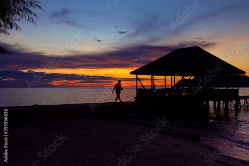 beach with footbridge to the sea at sunset with the silhouette of a person walking © Daniel