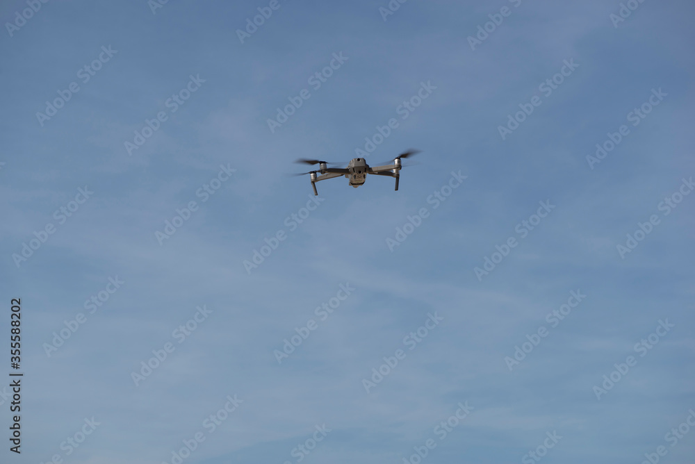 Drone flying in blue sky with clouds in the background. Drone flying overhead in cloudy blue sky. Drone quad copter with high resolution digital camera on the sky. Drone flying in blue sky with clouds in the background. Drone flying overhead in cloudy blue sky. Drone quad copter with high resolution digital camera on the sky.