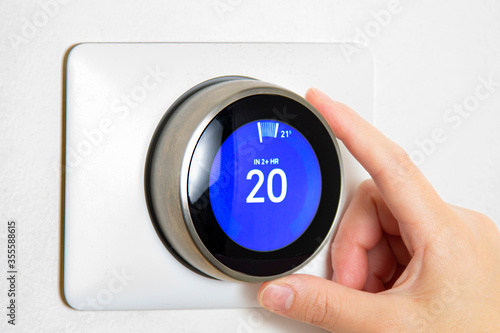 A person cooling down Home Air Conditioning, temperature is on centigrade celsius metrics using a smart thermostat on a white wall.