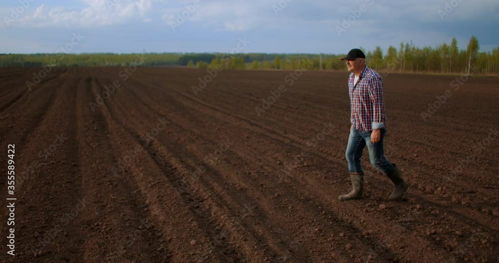 A male farmer walks through a field with plowed land in his boots in slow motion A male farmer walks through a field with plowed land in his boots in slow motion