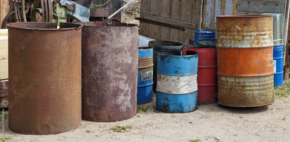 Rusty iron barrels stand on the ground near a village fence panorama Rusty iron barrels stand on the ground near a village fence panorama